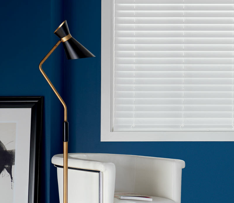 white composite blinds next to white fabric chair and modern lamp