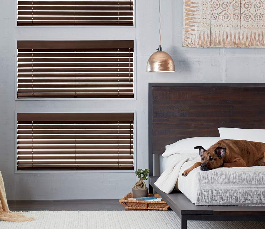 Bedroom with three windows covered with dark wood blinds from Hunter Douglas