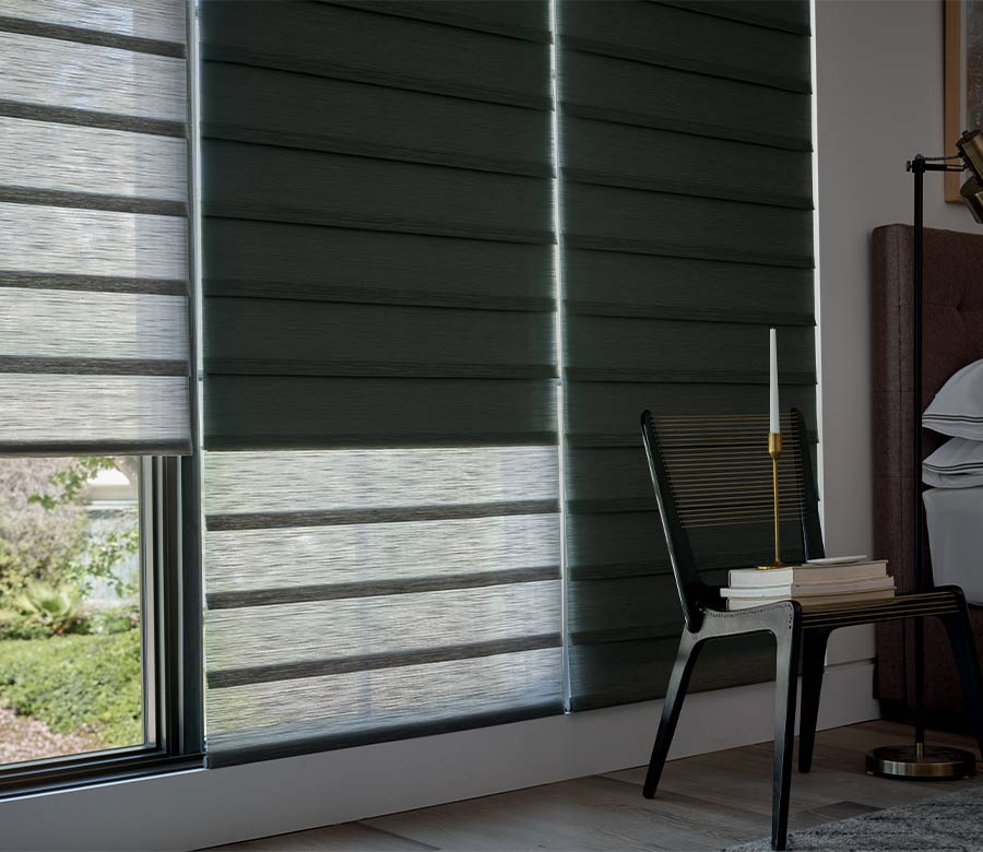 bedroom darkened by roller shades with woven backed chair with stacks of books