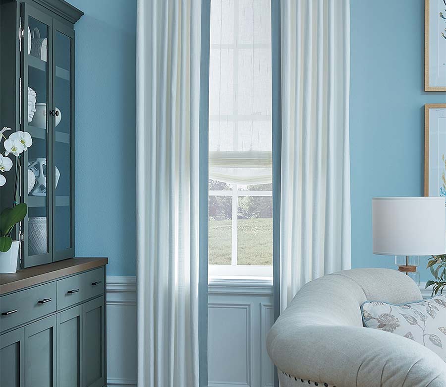 white draperies with blue edge banding layered with sheer white roman shades